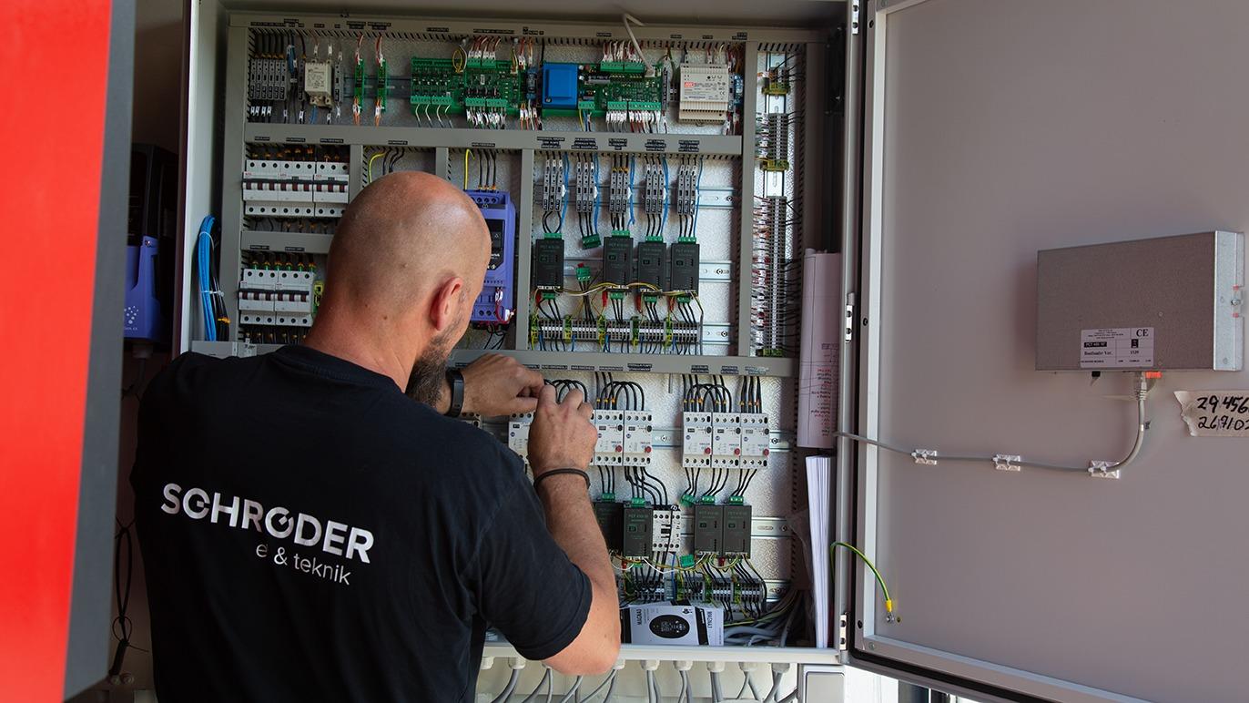 En tekniker arbejder med elektriske komponenter i et kontrolskab med ledninger og kredsløb.