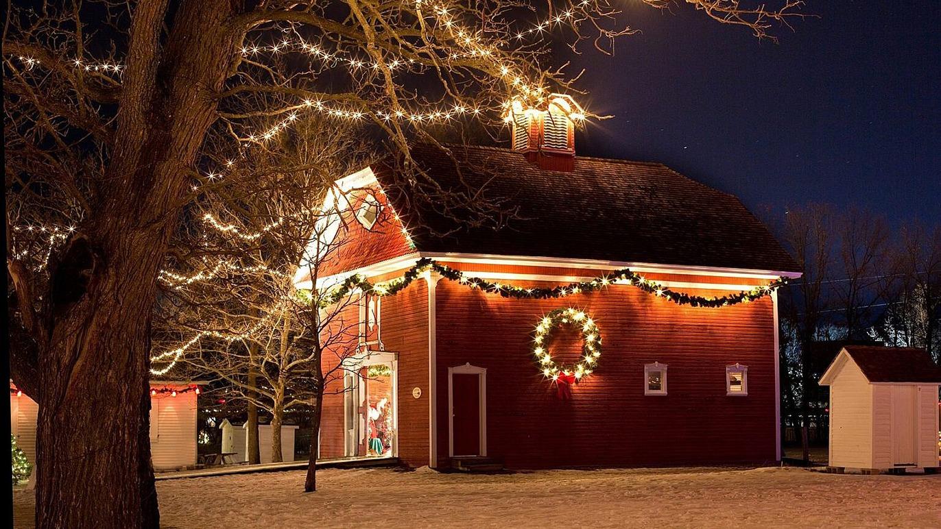 En rød lade pyntet med julelys og kranse, omgivet af nøgne træer om natten.
