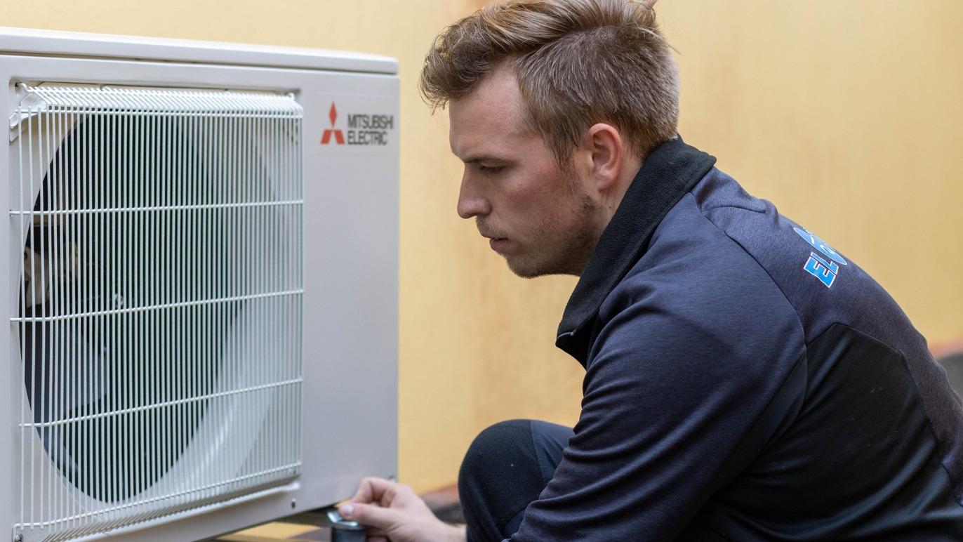 En tekniker arbejder på en udendørs airconditionenhed fra Mitsubishi.