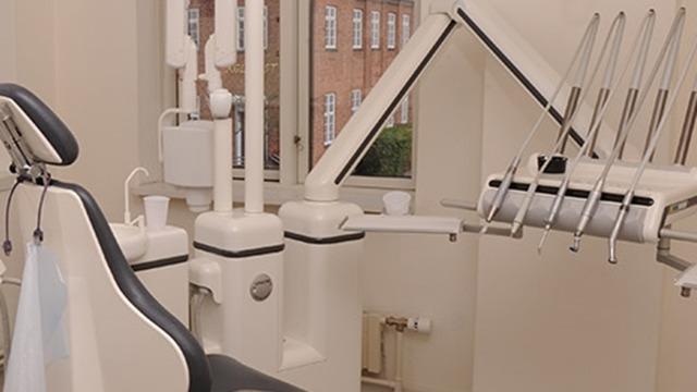 Moderne tandlægeklinik med tandlægestol, udstyr og vinduer, der giver naturligt lys.
