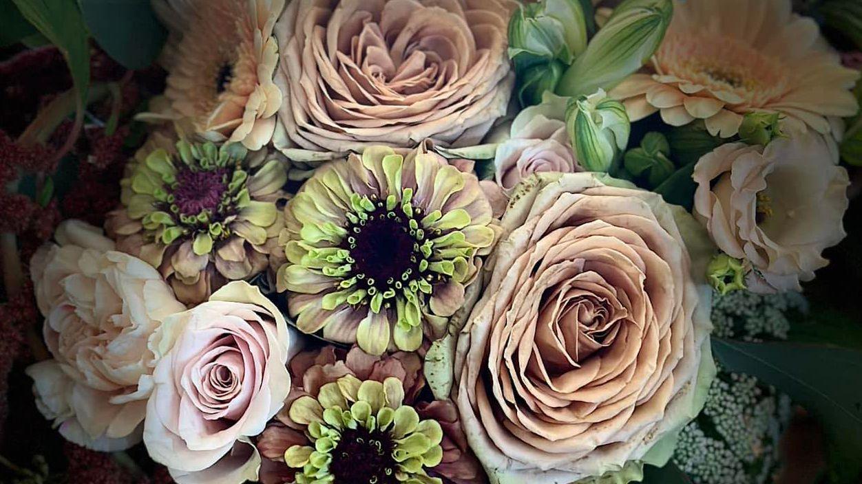 En smuk buket med roser, zinniaer og andre blomster i bløde nuancer af rosa og grøn.