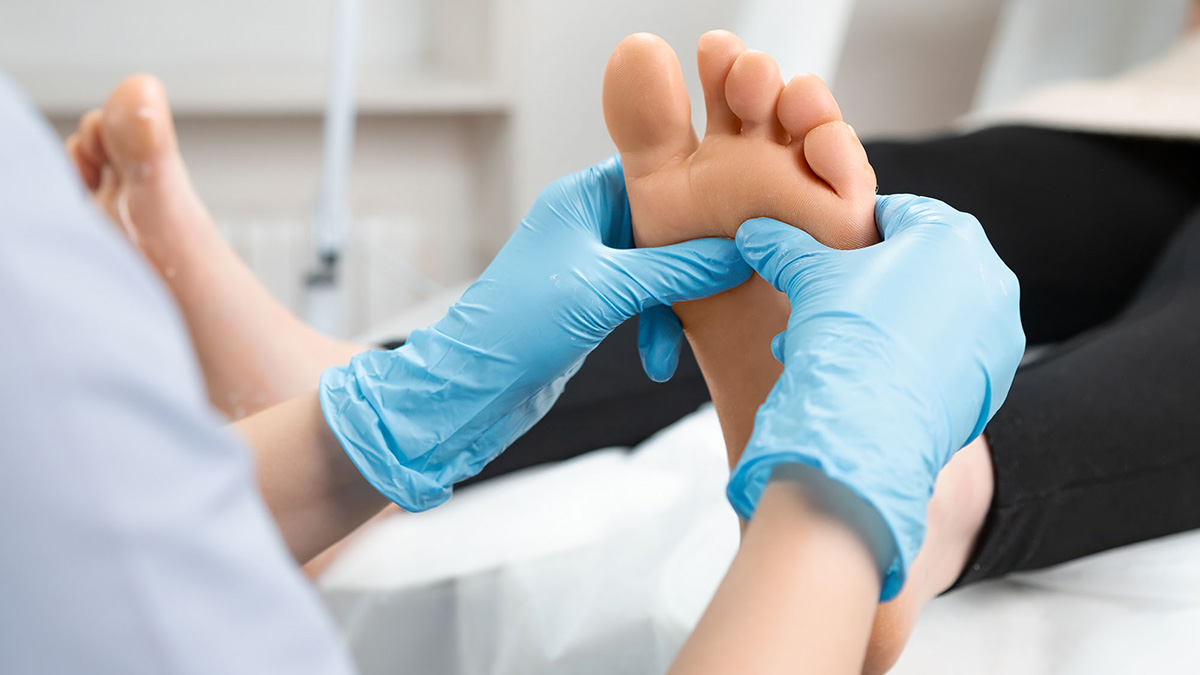 En person får fodmassage af en behandler iført blå handsker på en klinik.