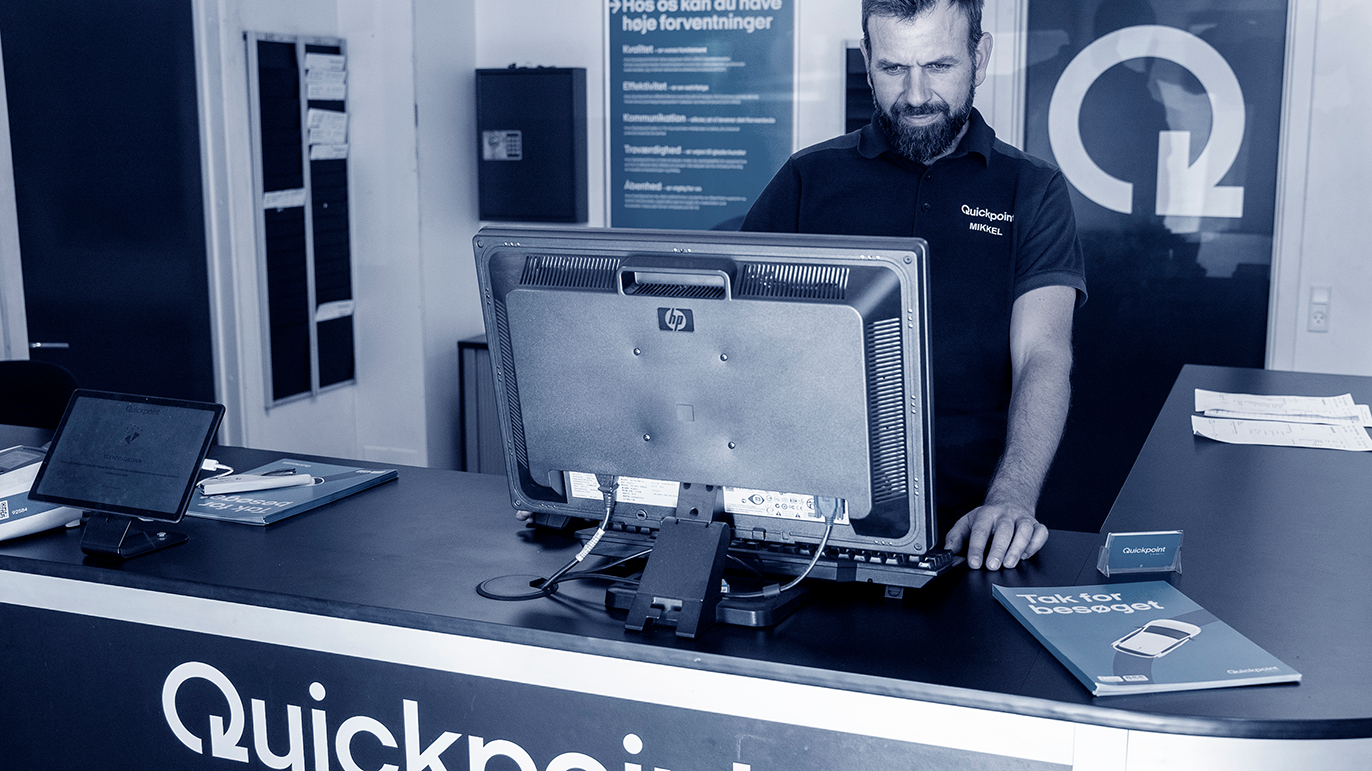 En mand står ved en reception med en computer og brochurer fra Quickpoint.