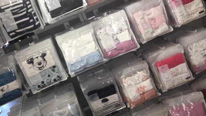 Hylder med pakker af baby tøj i forskellige farver og mønstre, herunder Mickey Mouse design.