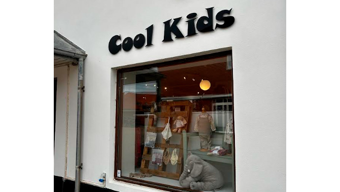 Butiksvindue med skiltet "Cool Kids" og udstillede børnetøj og legetøj.