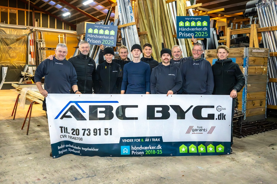 Gruppe af medarbejdere fra ABC BYG, der står foran en banner med virksomhedens kontaktoplysninger og priser.