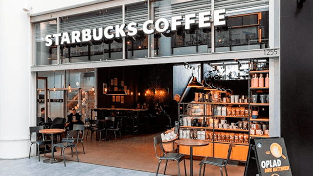 En Starbucks café med åbne døre, udendørs siddepladser og en hylde med kaffeprodukter.