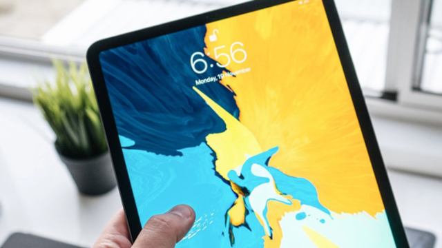 En person holder en tablet med en farverig skærm, der viser klokken 6:56 og en plante i baggrunden.