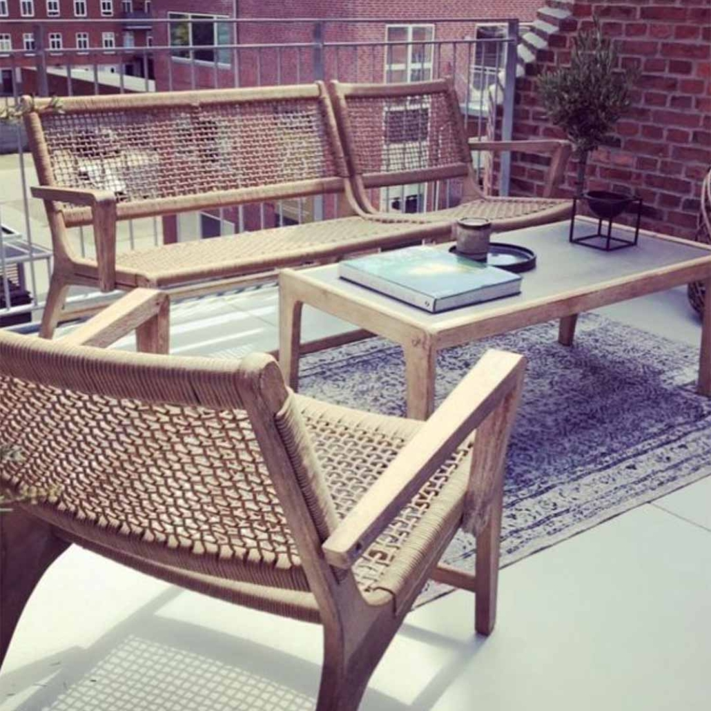 En hyggelig terrasse med en rattan sofa, et bord og en plante i en potte på et tæppe.