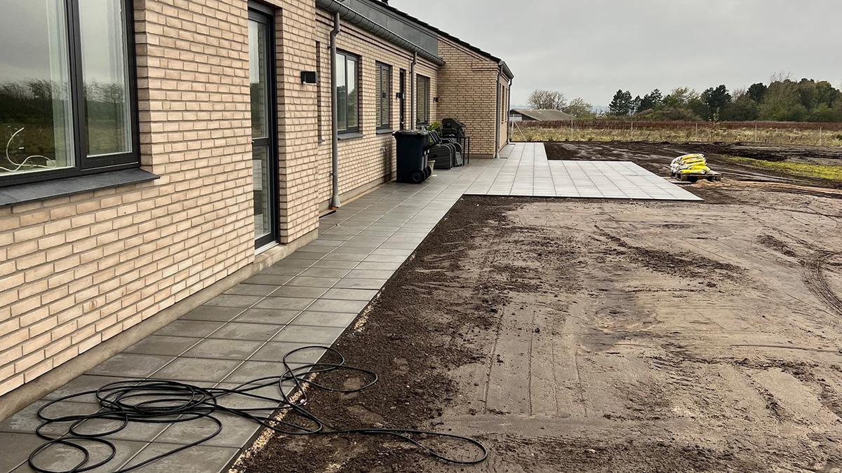 Nybygget hus med flisebelagt terrasse og grusareal, der er under opbygning, i et landligt område.