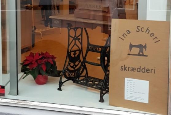 Vinduet til en skrædderbutik med en gammel symaskine og en rød julestjerneplante.