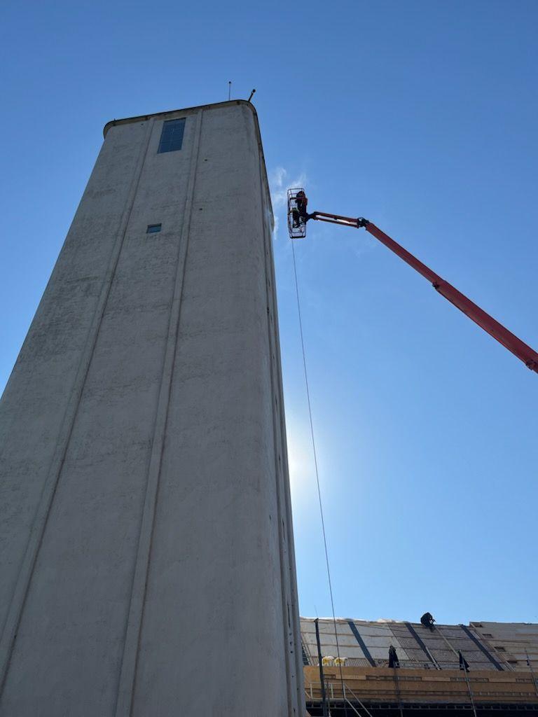 Arbejder på en høj bygning med en kran, der strækker sig mod en klar blå himmel.