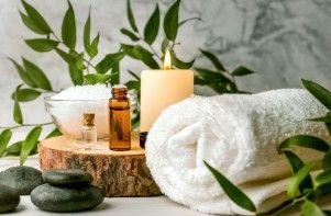Et afslappende spa-arrangement med håndklæde, æteriske olier, lys, salt og grønne planter på en træskive.