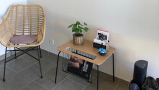 En moderne stue med en rattan stol, et træbord med planter og magasiner samt en sort vase.