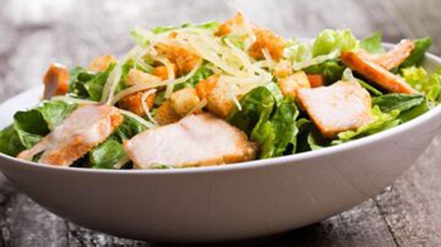En skål med salat, grillet kylling, croutoner og strimlet grøntsager på en træoverflade.