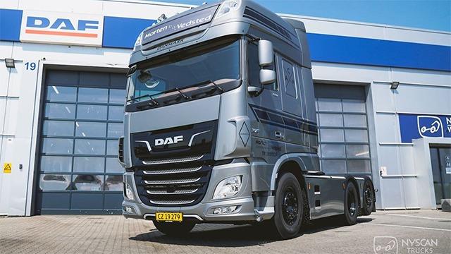 En sølvfarvet DAF lastbil parkeret foran en garage med åbne porte.