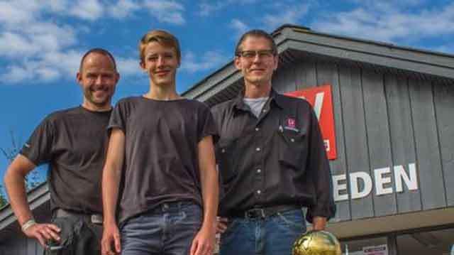 Tre personer står foran en bygning med et skilt, der viser navnet "Eden" under en blå himmel.