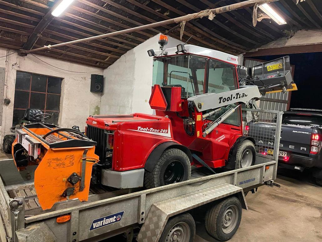 Rød gummiged på en trailer i en garage med værktøj og biler i baggrunden.