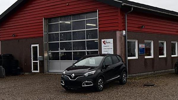 En sort Renault bil parkeret foran en rød bygning med store vinduer og en garageport.