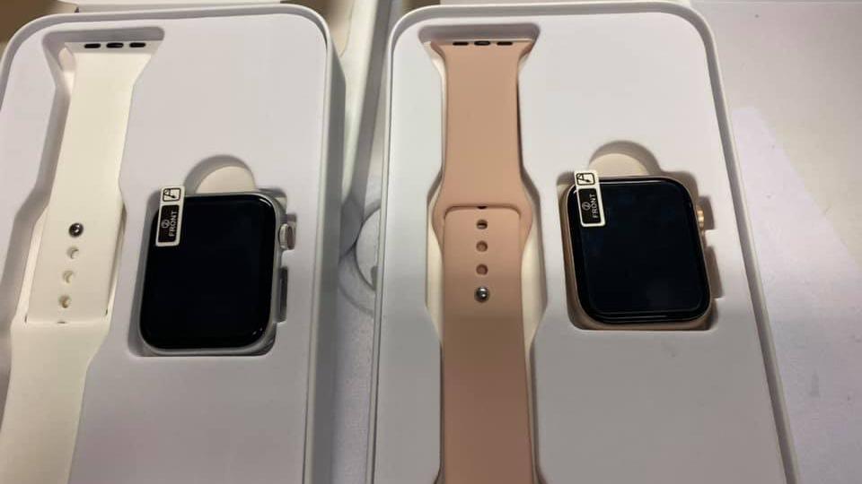 To smartwatch i hvid og lyserød i æske med remme, der viser skærmen og knapperne på siden.