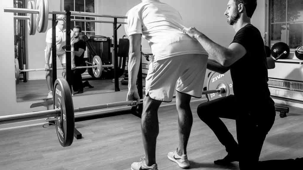 En personlig træner hjælper en mand med at løfte vægte i et fitnesscenter.