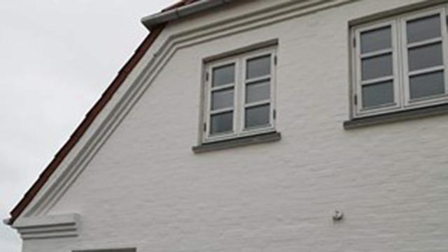 Hvidt hus med skråtag og vinduer på første sal under en grå himmel.