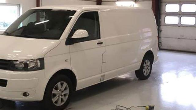 Hvid varevogn parkeret i en garage med lys gulv og åbne garageporte.