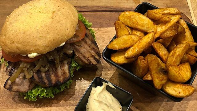 En saftig burger med salat, tomat og løg, serveret med sprøde kartoffelbåde og en skål mayonnaise.