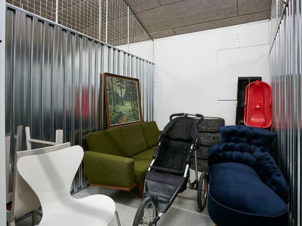 Lagerlokale med en grøn sofa, en barnevogn, en rød kasse og en maleri på væggen.