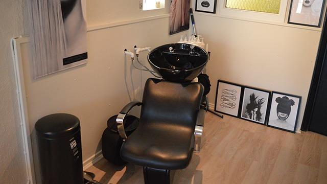 En frisørsalon med en sort vask, en stol og vægkunst i rammer.