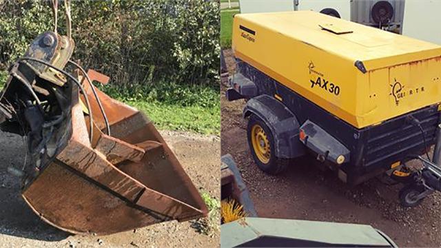 Billede af en rusten skovl og en gul kompressor på en trailer, begge står på en grusvej omkranset af vegetation.
