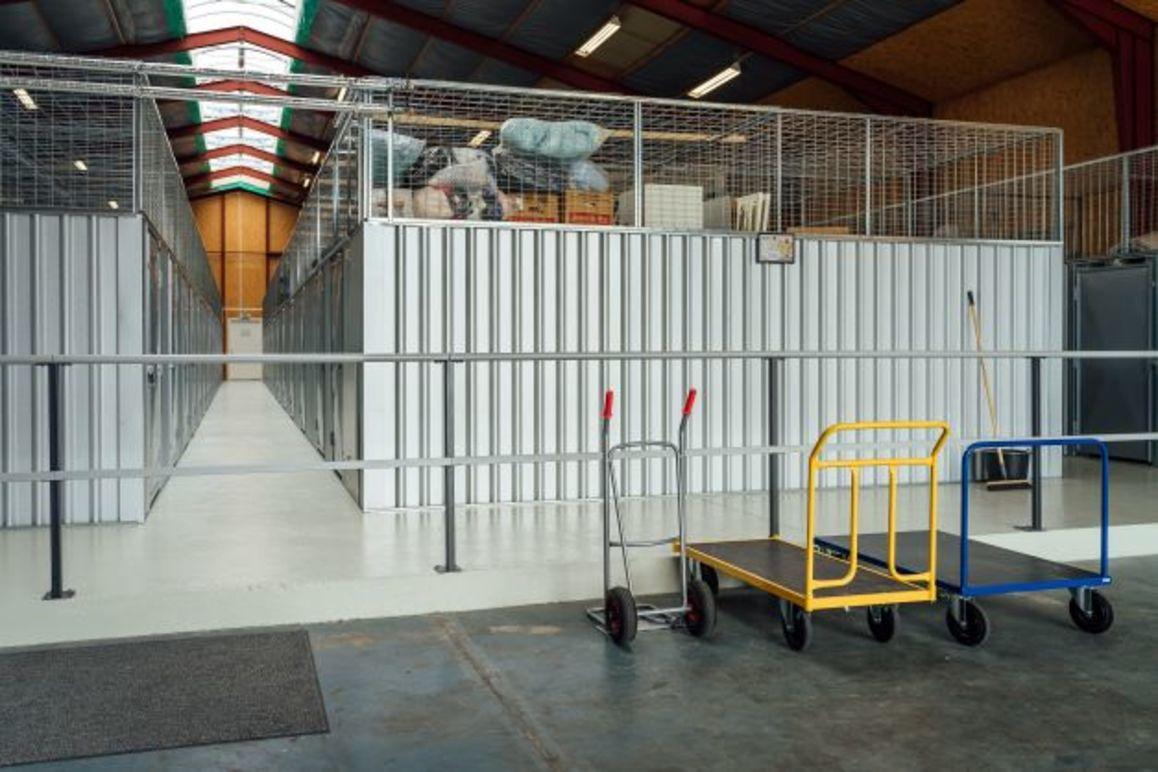 Lagerområde med opbevaringsrum og transportvogne i forgrunden.