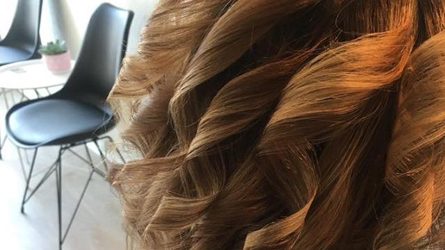 En tæt frisørfrisure med bløde, bølgede krøller i brunt hår, set fra siden i en moderne salon.