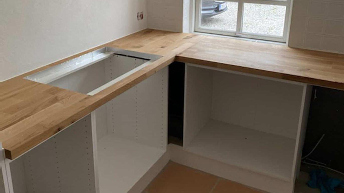 Køkkenbord med træoverflade og åbning til vask, samt hvidt skab uden indhold.