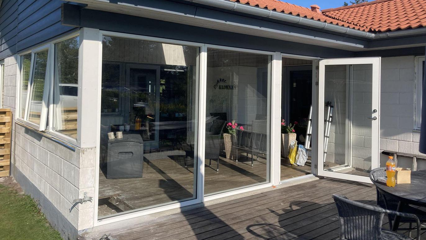 En moderne terrasse med store glasdøre, der fører ind til stuen i et hus med rød tag.