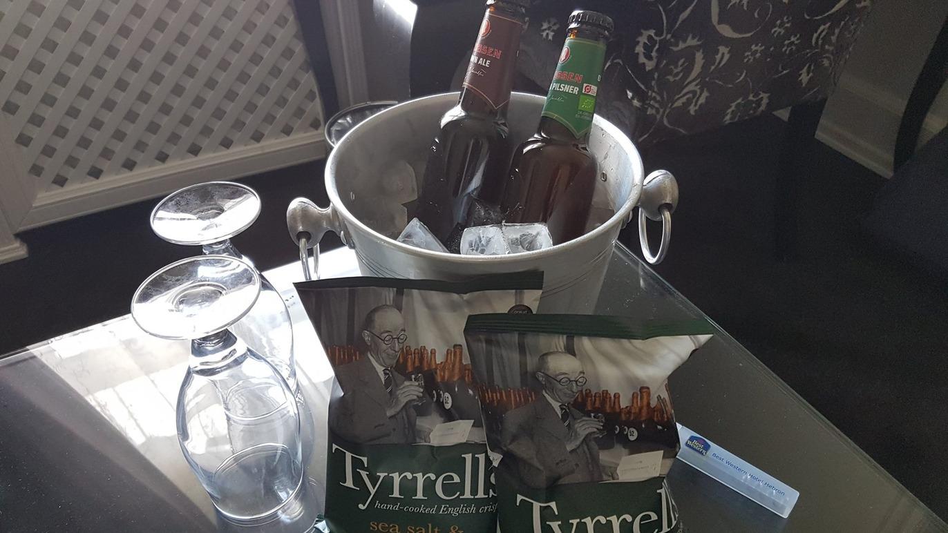 En køler med ølflasker, glas og en pose Tyrrell's chips på et bord.
