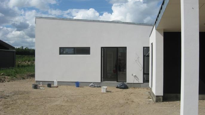 Moderne hus med hvid facade og store vinduer, omgivet af sand og malerskåle.