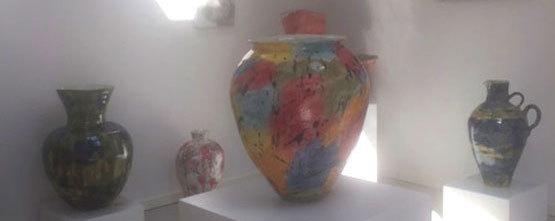 Farverige keramikvaser i et kunstgalleri, herunder en stor vase med abstrakte mønstre og mindre vaser i forskellige farver.