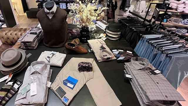 En tøjbutik med skjorter, bukser, sko og accessories præsenteret på et bord.