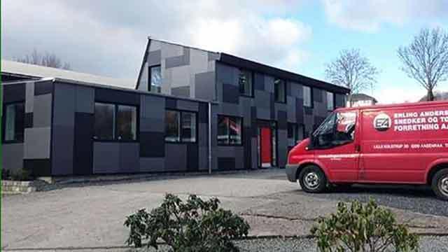 Moderne bygning med grå og sorte facader og en rød varevogn parkeret foran.
