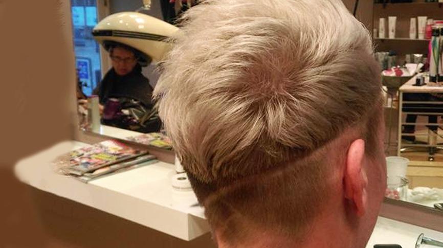 En person med kort, lys hårfrisure og en skarp hårgrænse, der sidder i en frisørsalon.