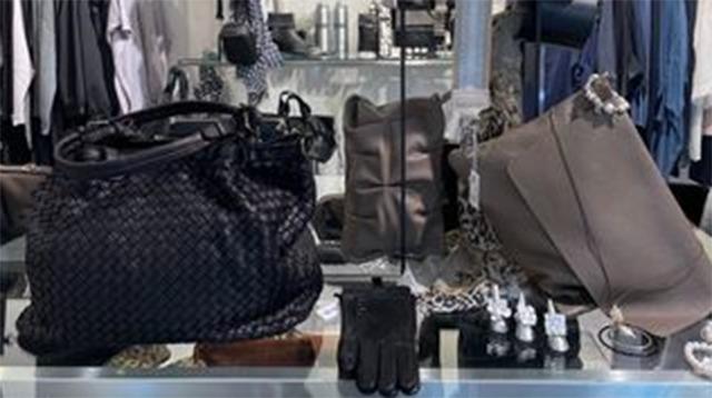 Billede af en modebutik med sorte og grå tasker samt handsker og accessories på et glasbord.