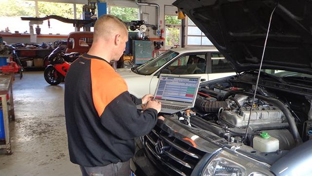 Mekaniker arbejder på en bil i et værksted, mens han bruger en bærbar computer til diagnosticering.