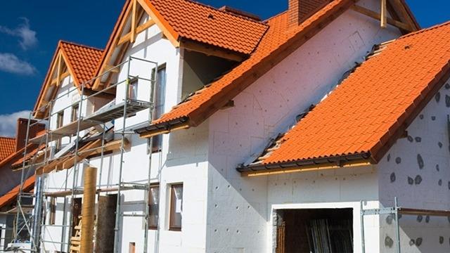 Hus under konstruktion med røde tagsten og stillads, der viser byggeri og renovering.