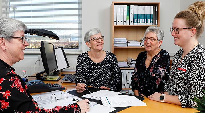 Fire kvinder i kontormiljø, der diskuterer dokumenter og arbejder sammen ved et skrivebord.
