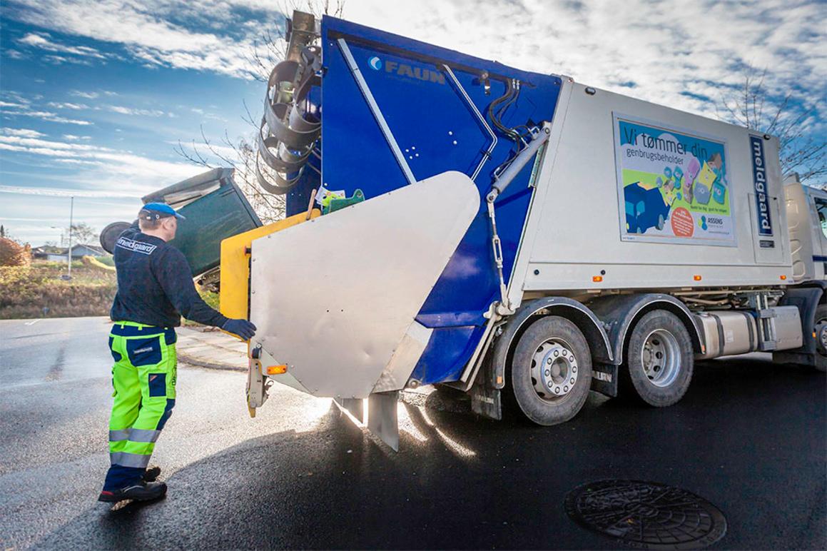 En skraldemand tømmer affald i en affaldscontainer fra en skraldebils bagagerum på en solrig dag.