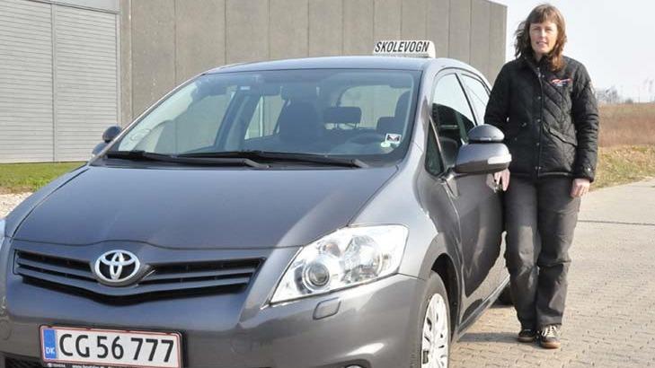 En kvinde står ved siden af en grå taxa med et skilt på taget, parkeret på en vej.