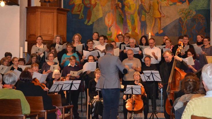 En korgruppe synger med noder, mens en dirigent leder dem i en kirke med farverig vægmaleri.