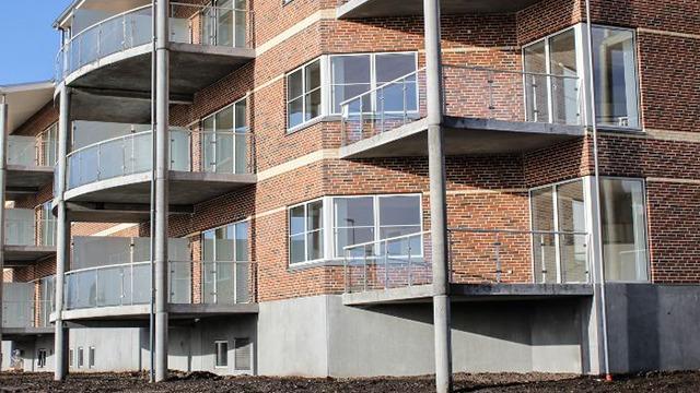 Moderne lejlighedsbygning med store altaner og murstensfacade. Sollys reflekteres i vinduerne.