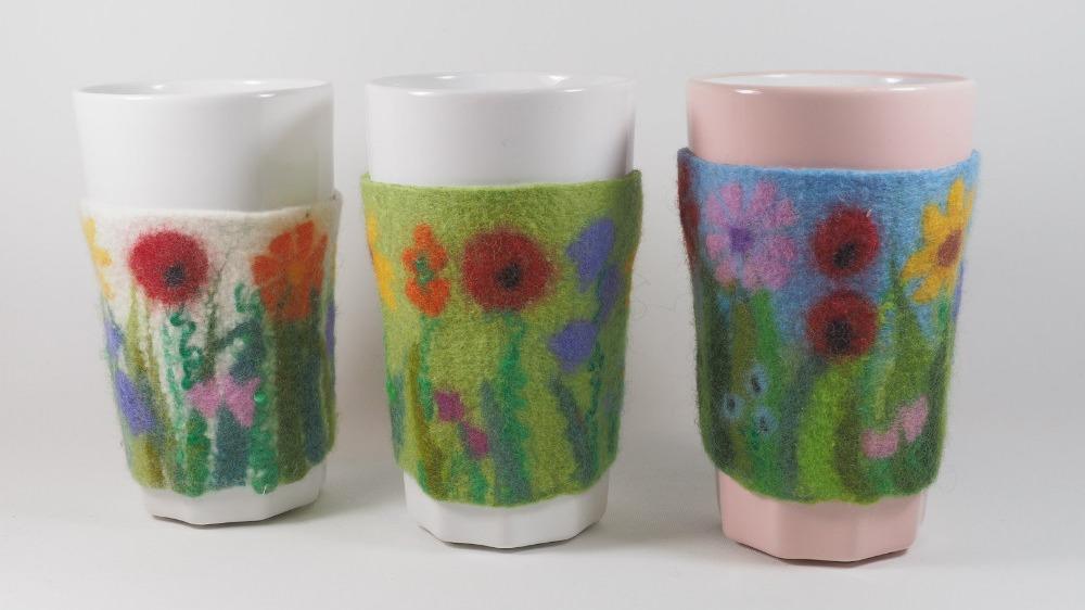 Tre krus med farverige filtede omslag, dekoreret med blomster og grønne planter.